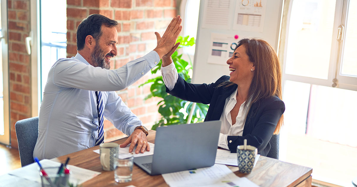 two business professionals high fiving each other over laptop