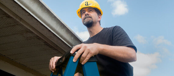 man in hard hat on blue ladder next to roof