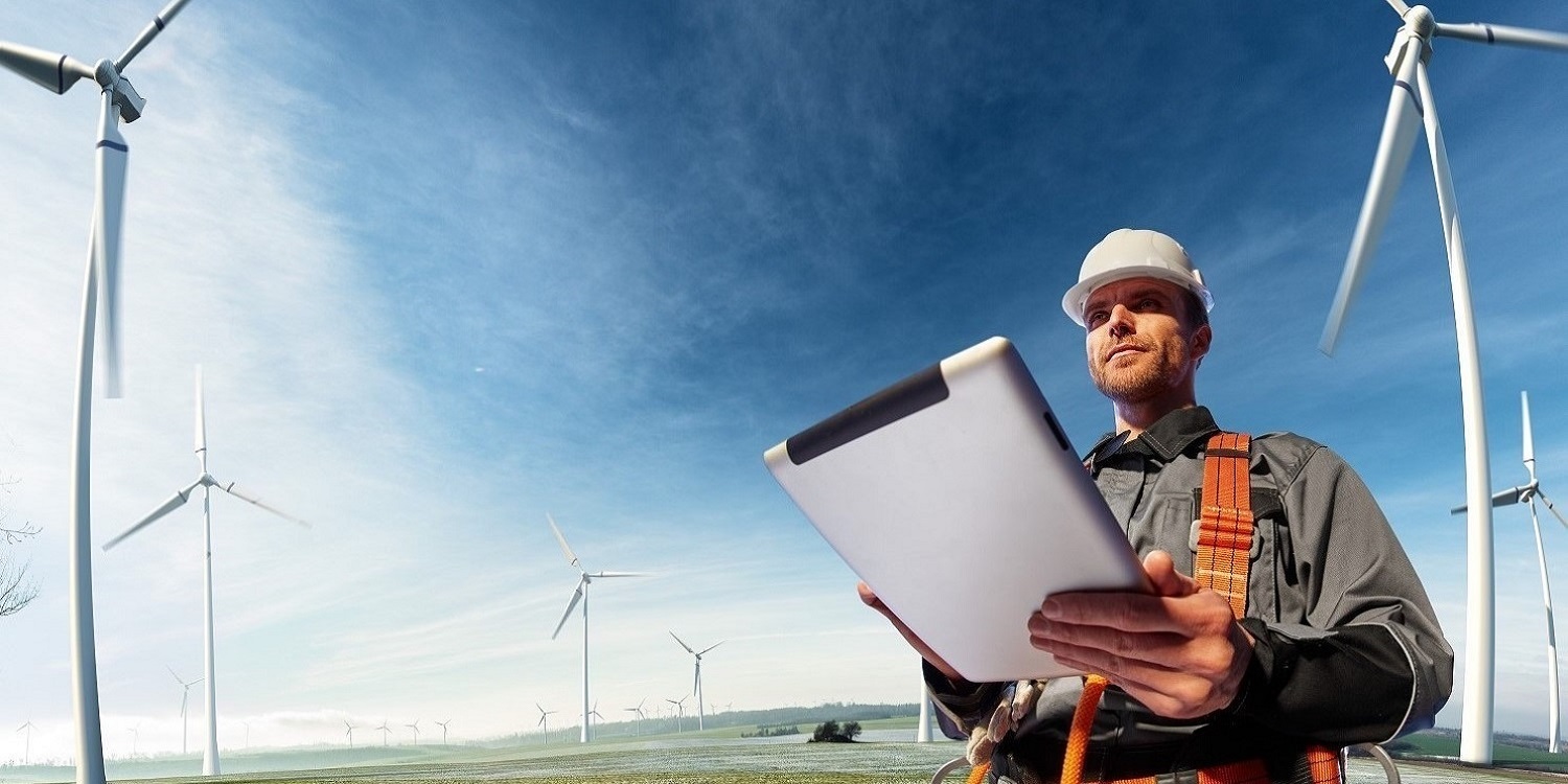 engineer with computer pad and hardhat on a background of windmills and blue sky
