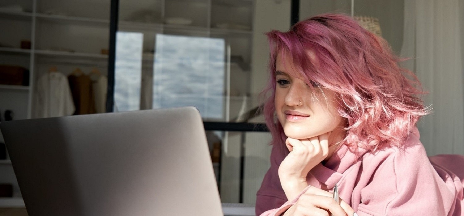 girl with pink hair and pink jacket laying down with laptop