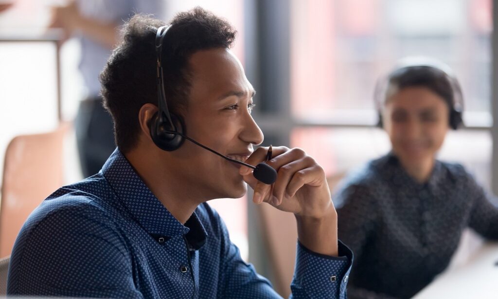man on headset smiling while another agent looks on