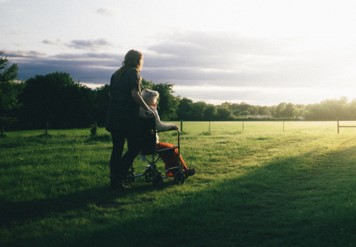 woman pushing elderly person across a field into the sunset