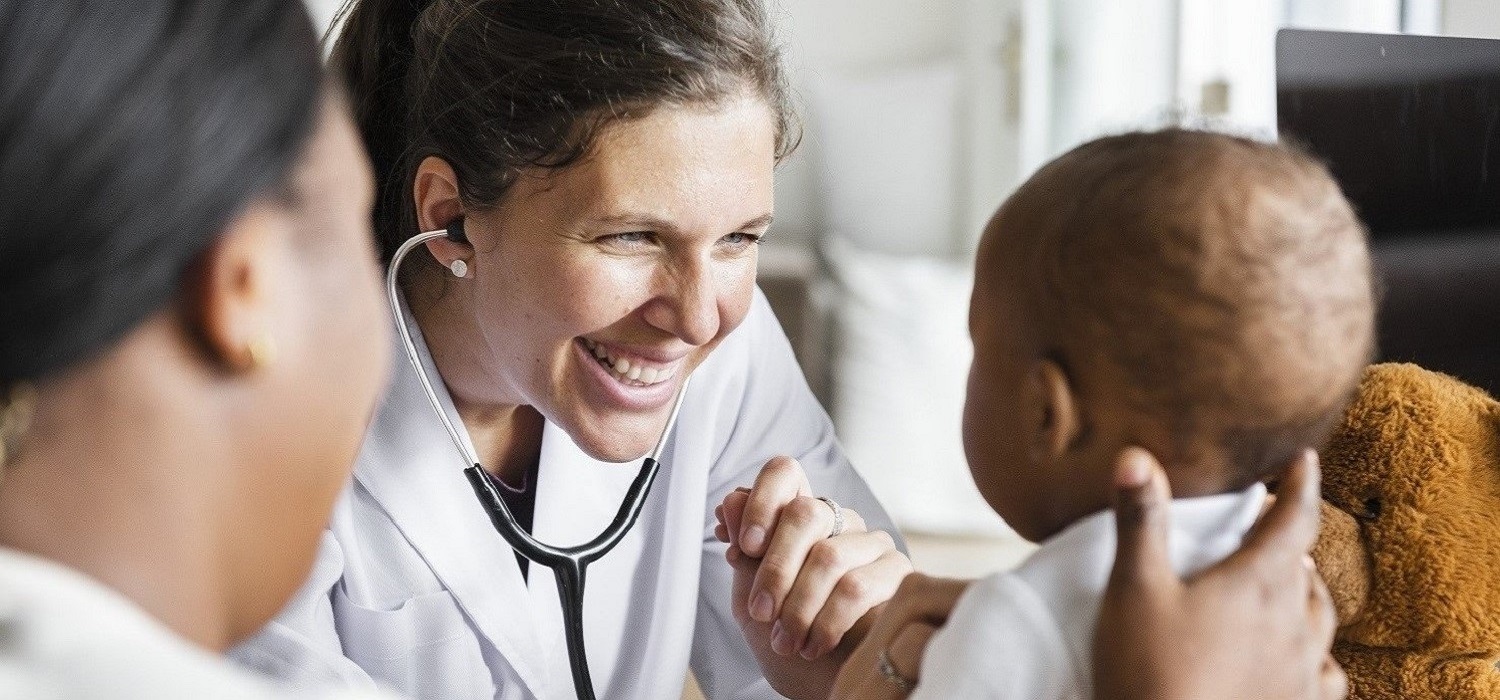 female doctor smiling at baby while checking his heartbeat