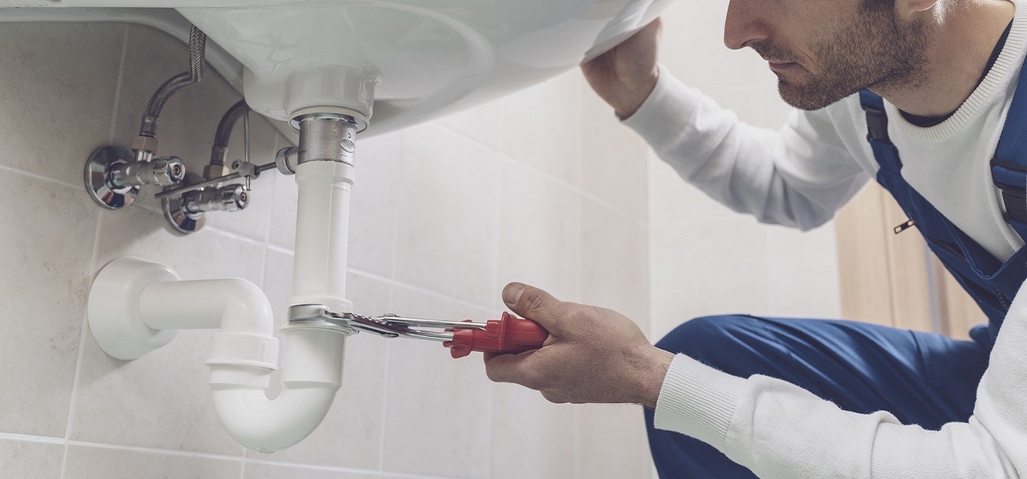 plumber in white suit under a sink tightening a pipe