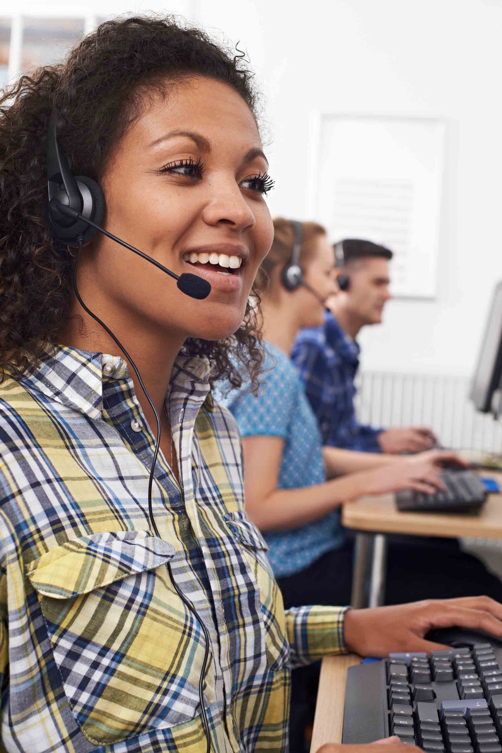 woman in plaid shirt with headset at desk and other agents next to her