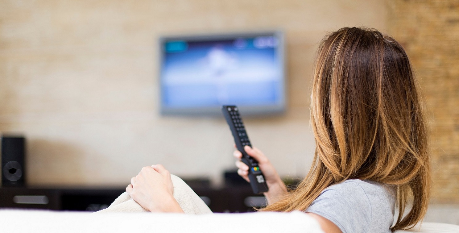 Woman on couch with remote in hand in front of tv